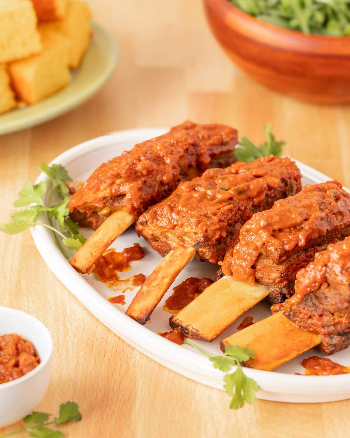 White platter holding 4 Spicy Beef Ribs with cornbread and salad in the back